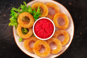 Calamari rings close-up on black. Squid rings with green salad leaves and a dip, top shot on a dark background