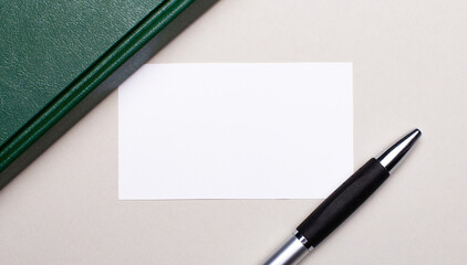 On a light gray background lies a pen, a green notebook and a white blank card with a place to insert text. Business concept. Template