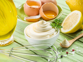 Bowl with mayonnaise sauce in the centre and mayonnaise ingredients around it on wooden table.