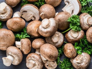 Brown colored edible mushrooms or cremini mushrooms on wooden table with herbs. Top view.
