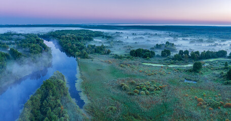 Smoky morning mist over the river. Beautiful panoramic view of river and green banks of the river in the early summer morning.