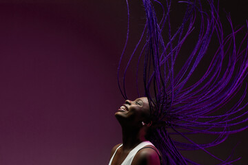 Minimal portrait of African-American woman dancing against purple background with purple braids in air, copy space