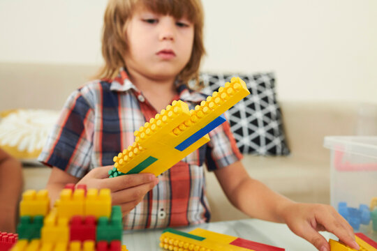 Concentrated little boy playing with colorful toy bricks in playroom