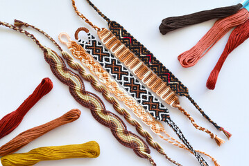 Woven DIY friendship bracelet with brown patterns next to skeins of embroidery floss