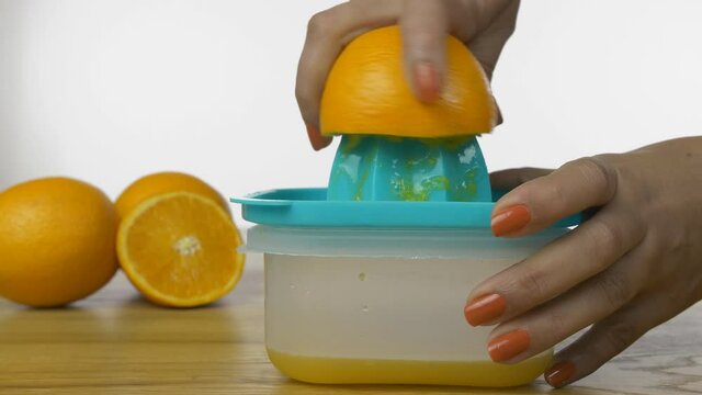 Closeup shot of woman hands squeezing out fresh orange juice on a manual juicer. Hands of an Indian female juicing orange fruit on a manual plastic squeezer against the white background