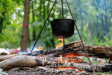Camping outdoors. Cooking bowler hat hung on tripod over bonfire