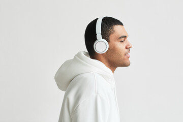 Minimal side view portrait of modern Latin American man wearing headphones white hoodie while...