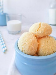 Vegan coconut cookies with cracks in a blue ceramic bowl close-up on a light background side view. A delicious snack for children and adults, dessert and a glass of milk.