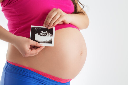 Pregnant woman holding ultrasound scan photo of her baby isolated