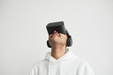 Minimal portrait of modern young man wearing VR headset against white background and looking up, copy space