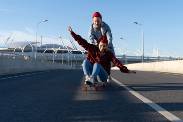 Carefree hipsters couple skateboarding together. Trendy casual man and woman have fun riding longboard skate down empty street, cheerful lovers spend time outdoors chilling. Youth and freedom concept