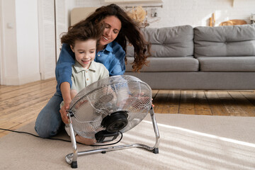 Parent and kid at home: cheerful young mum with small son enjoy propeller fan indoors. Single...