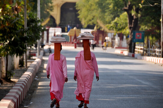 Burmese nuns women put holding tray on head walking on street at beside road front of ancient ruins building of Mandalay Palace go to Paya pagoda temple in Mandalay, Myanmar or Burma