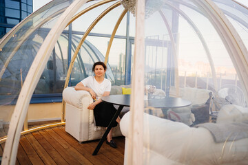 woman in a white t-shirt sits at tables in a cafe in shape of a igloo on roof