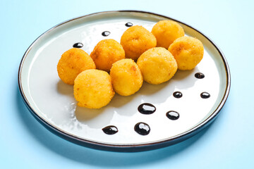 Plate with fried potato balls on color background