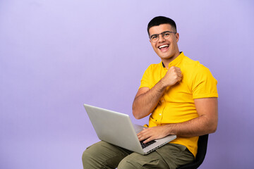 Young man sitting on a chair with laptop celebrating a victory