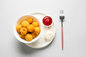 Bowl with fried potato balls on light background