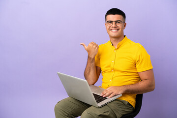 Young man sitting on a chair with laptop pointing to the side to present a product