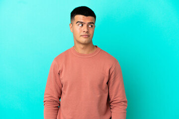 Young handsome man over isolated blue background making doubts gesture looking side