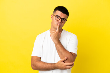 Young handsome man over isolated yellow background having doubts while looking up