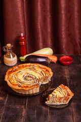 The cut piece of Vegetable Spiral tart with zucchini, eggplant, carrot on wooden background