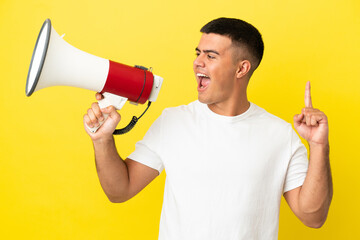 Young handsome man over isolated yellow background shouting through a megaphone to announce something in lateral position