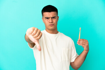 Young handsome man brushing teeth over isolated blue background showing thumb down with negative expression