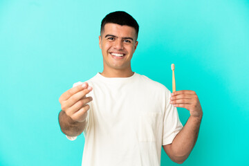 Fototapeta premium Young handsome man brushing teeth over isolated blue background making money gesture