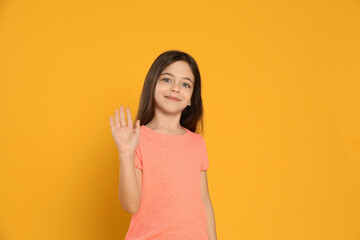 Happy little girl waving to say hello on yellow background © New Africa