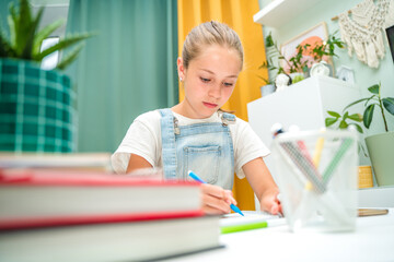 A beautiful little girl is studying at a cozy desk with books. School education at home or preparing for school on vacation