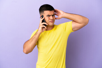 Young handsome man using mobile phone over isolated purple background having doubts