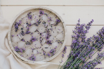 Ice cubes with lavender in glasses standing on a marble tray on wooden background.