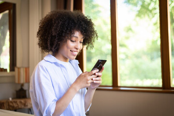Satisfied hipster girl with Afro haircut, types text message on cell phone, enjoys online communication, types feedback