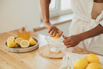Young woman making lemonade in a kitchen of cozy house. Homemade healthy drink. - obrazy, fototapety, plakaty