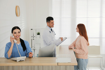 Receptionist talking on phone while doctor working with patient in hospital