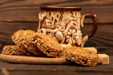 Homemade cookies with sunflower seeds and raisins, pieces of brown cane sugar and an earthenware mug of tea on a wooden table. Close-up Selective focus.