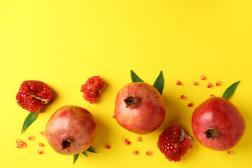 Ripe pomegranate, leaves and seeds on yellow background