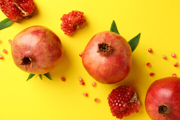 Ripe pomegranate, leaves and seeds on yellow background