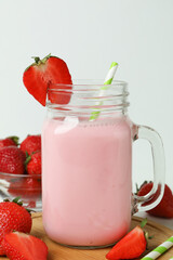 Glass jar of strawberry milkshake and ingredients on white background