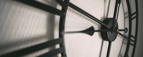 Pointer of large black clock hanging on white wall in afernoon