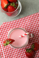 Glass jar of strawberry milkshake and ingredients on gray textured table