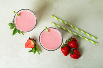 Glasses of strawberry milkshake and ingredients on white textured table
