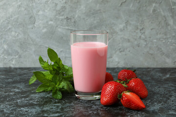 Glass jar of strawberry milkshake and ingredients on black smokey table