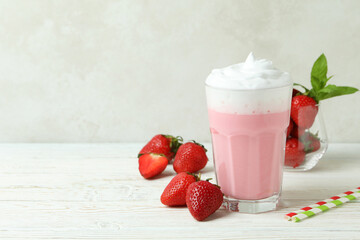 Glass of strawberry milkshake and ingredients on white wooden table