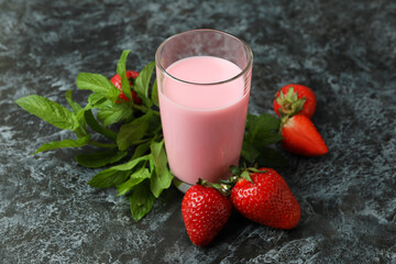 Glass jar of strawberry milkshake and ingredients on black smokey table