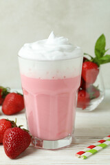 Glass of strawberry milkshake and ingredients on white wooden table