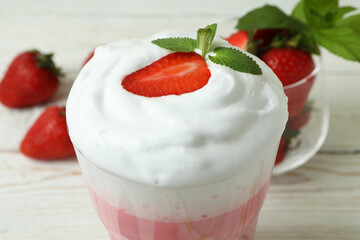 Glass of strawberry milkshake and ingredients on white wooden table