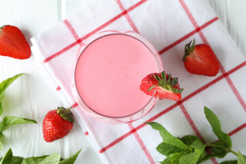 Glass jar of strawberry milkshake and ingredients on white wooden table