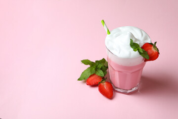 Glass of strawberry milkshake and ingredients on pink background
