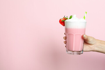Female hand holds glass of strawberry milkshake on pink background